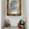 An antique mirror with golden decoration above a windowsill with decoration.