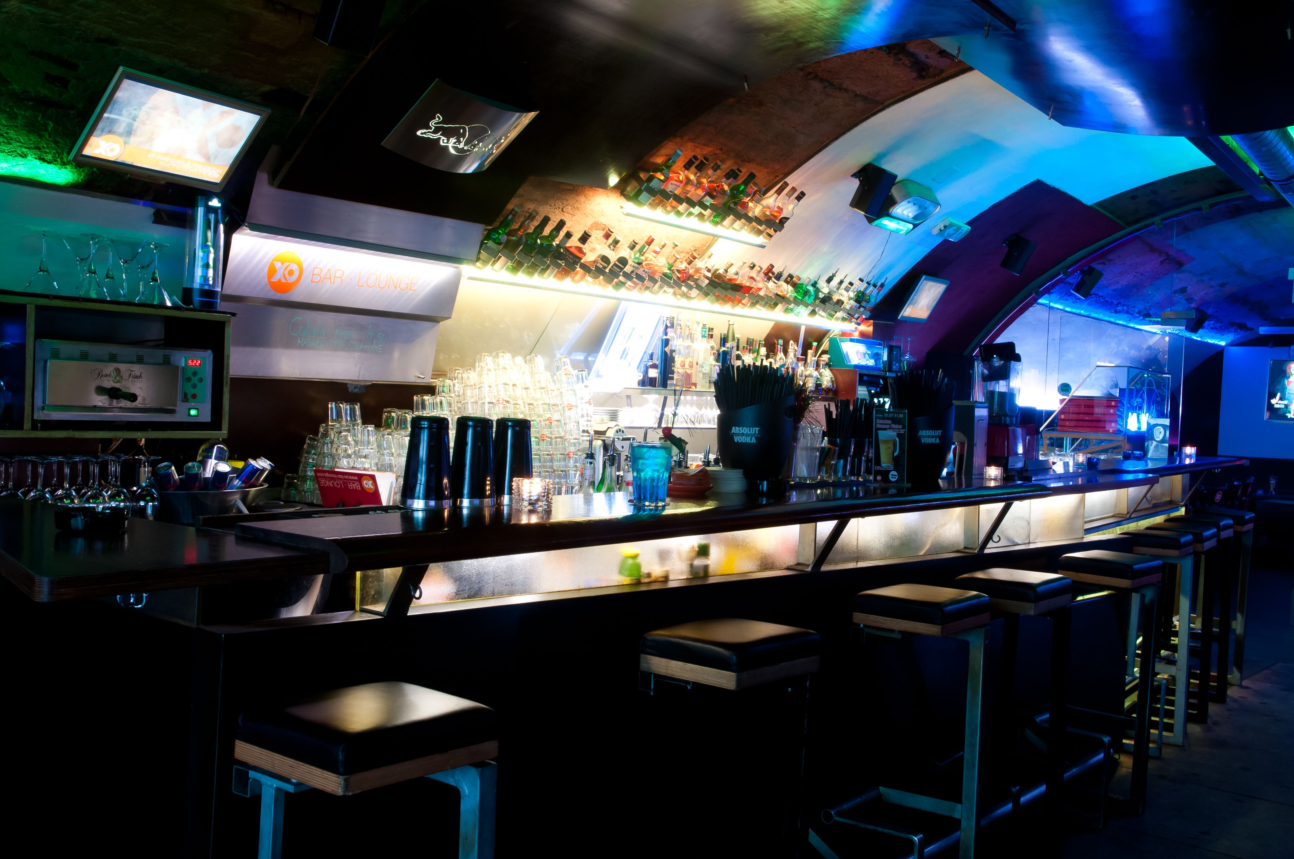 Innenansicht einer stilvollen Bar mit beleuchtetem Tresen und Barhockern.
