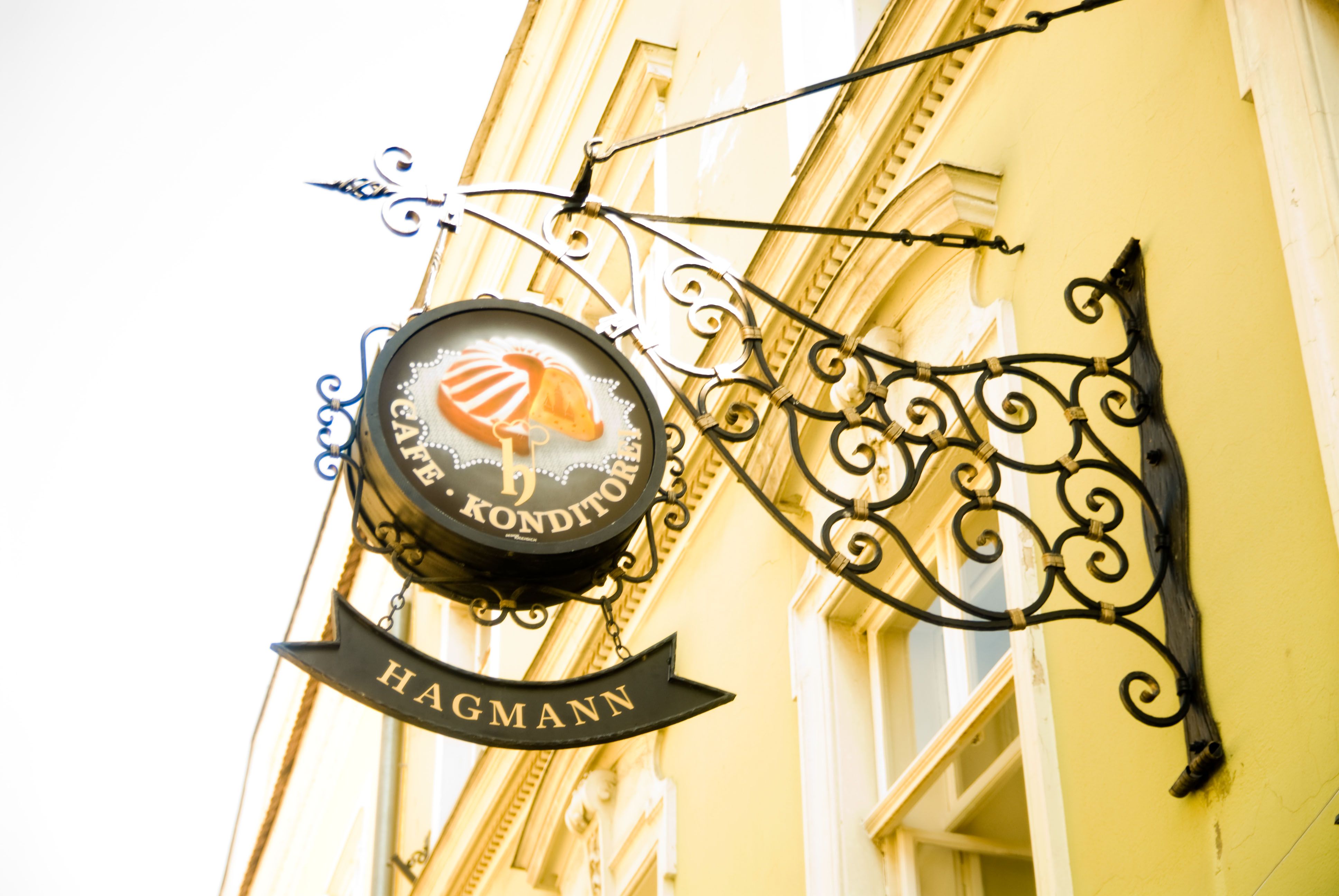 Metallschild 'Café Konditorei Hagmann' an einer gelben Hauswand.