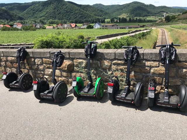 Sechs Segways stehen vor einer Steinmauer mit Landschaft im Hintergrund.