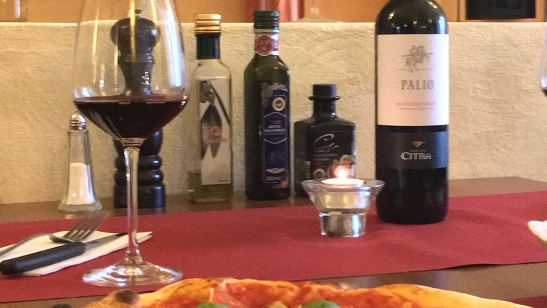 Pizza mit Basilikum und Parmesan auf einem Tisch mit Rotwein und Oliven&ouml;l.