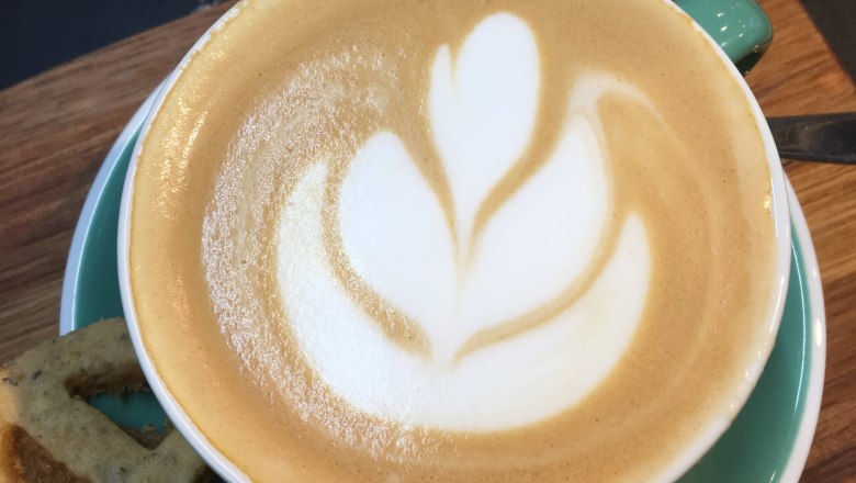 Cappuccino mit Latte Art in einer gr&uuml;nen Tasse auf einem Holzbrett.
