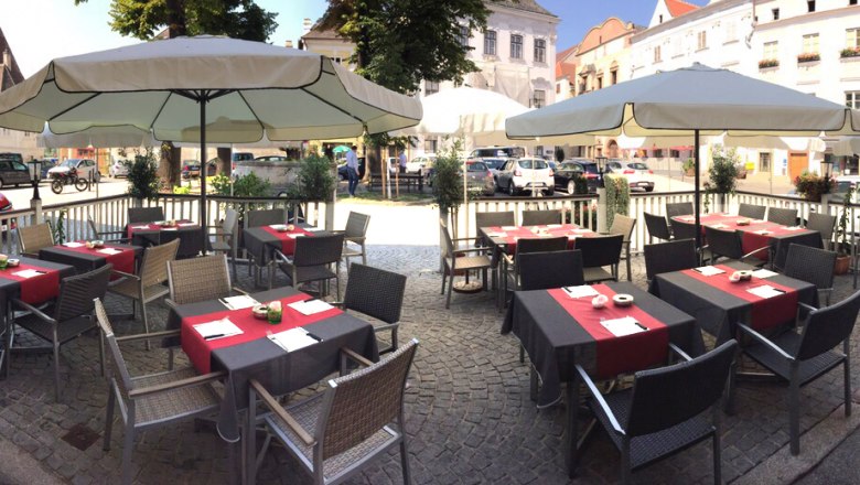 Outdoor terrace of a caf&eacute; with tables and parasols on a paved square.