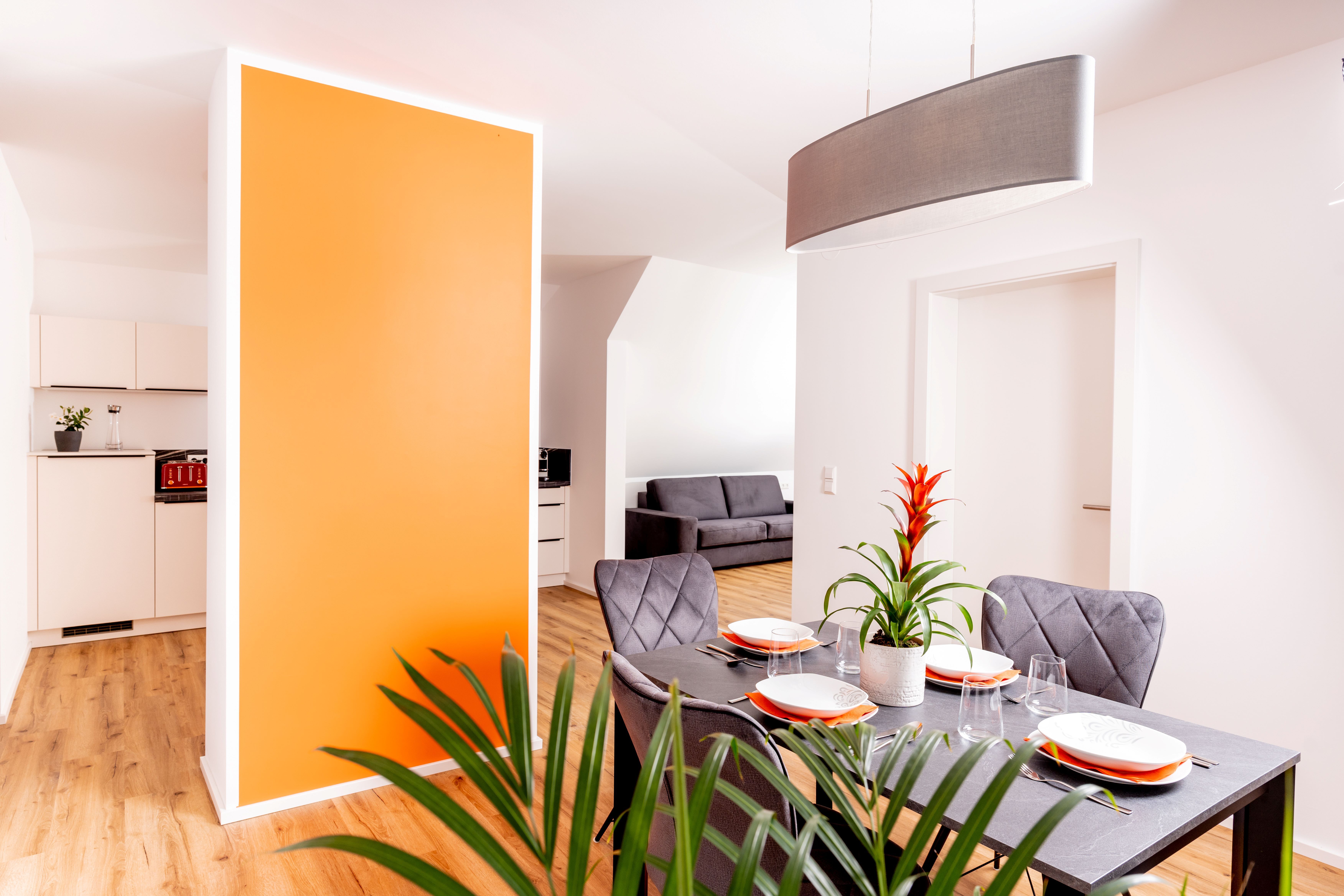 Moderne Ferienwohnung mit Essbereich, oranger Wand und grauem Sofa.