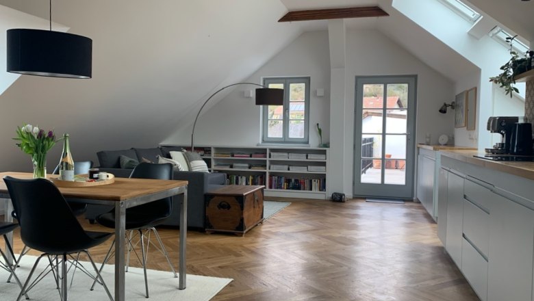 Modern attic apartment with wooden floor, dining table, sofa and access to a balcony.