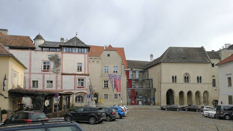 Historische Geb&auml;ude am Hohen Markt mit geparkten Autos auf Kopfsteinpflaster.