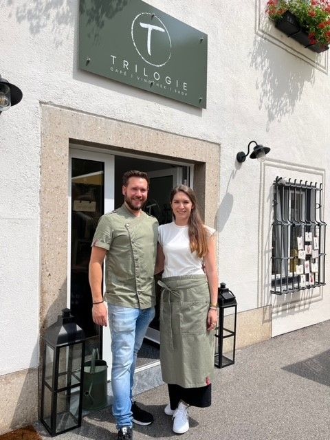 Ein Mann und eine Frau stehen vor einem Café namens Trilogie.