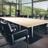 Modern seminar room with large wooden table and black chairs, surrounded by glass walls with a view of the green landscape.