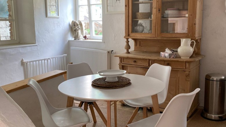 Dining area with round table, four white chairs, wooden cupboard and decoration in a bright room.