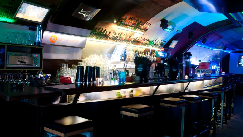 Innenansicht einer stilvollen Bar mit beleuchtetem Tresen und Barhockern.