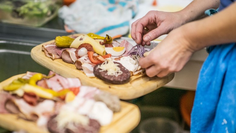 Person prepares a snack with sausage, cheese and vegetables.
