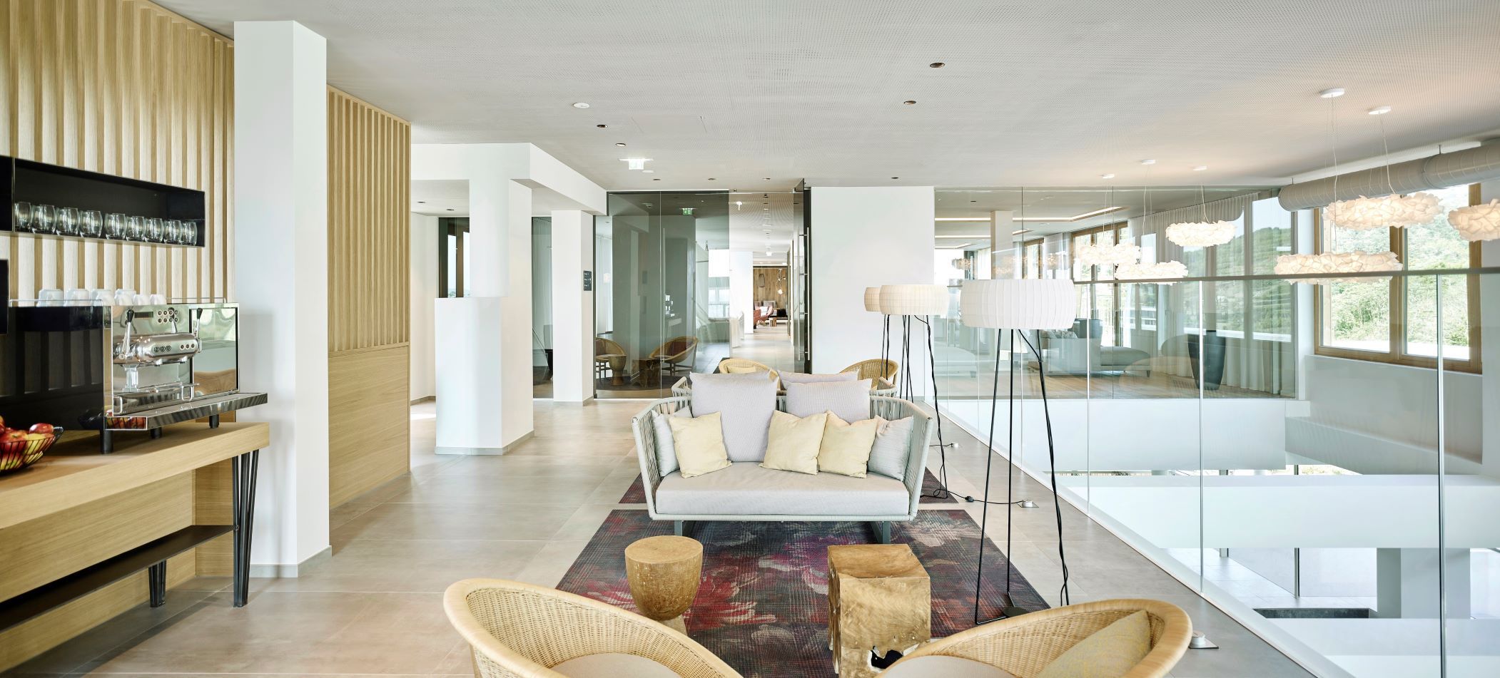 Moderner Aufenthaltsbereich im Hotel-Spa mit heller Einrichtung, Sofas, Stehlampen und einer Kaffeemaschine.