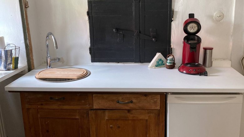 Small kitchen with wooden cupboards, white worktop, red coffee machine and small fridge.