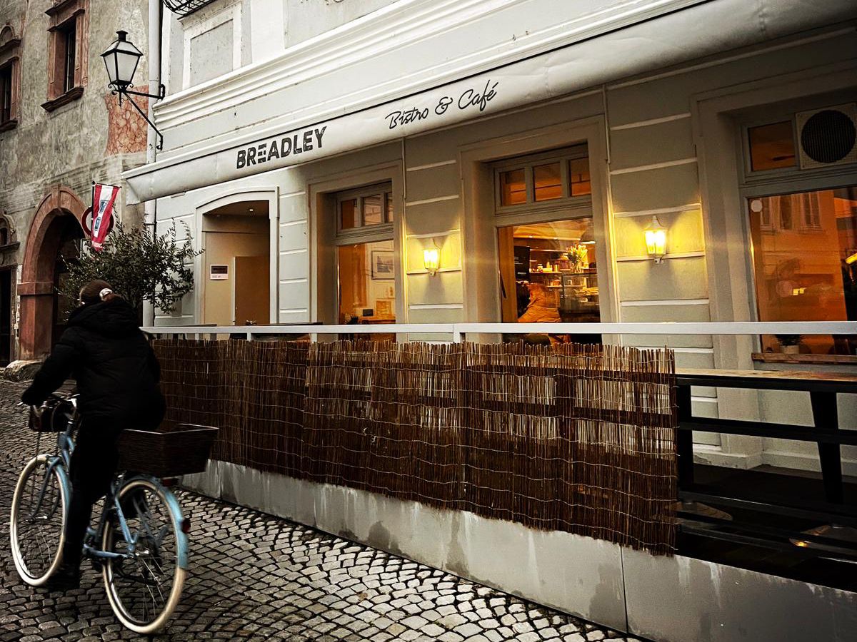Außenansicht eines Cafés mit einem Radfahrer auf Kopfsteinpflaster.