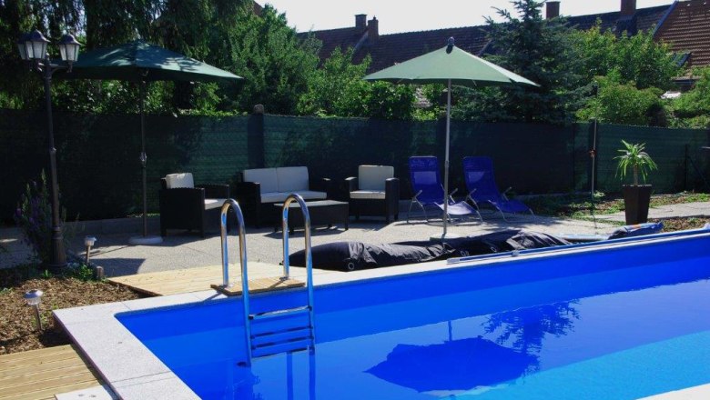 An outdoor area with a blue pool surrounded by sun loungers, parasols and garden furniture.