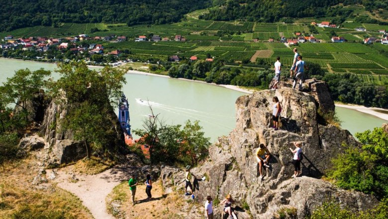 People climbing on rocks with a view of the Danube and vineyards in D&uuml;rnstein.