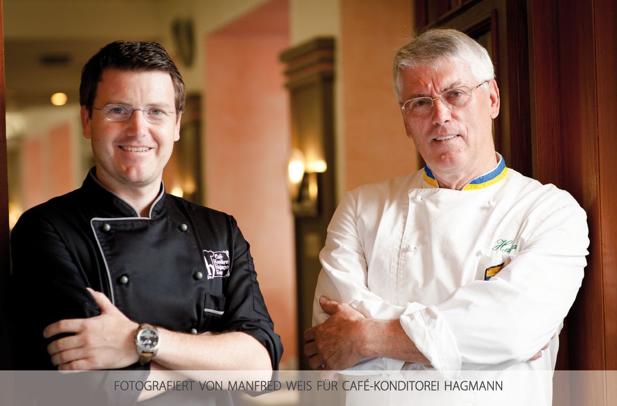 Zwei Männer in Konditoruniformen stehen nebeneinander und lächeln in die Kamera.