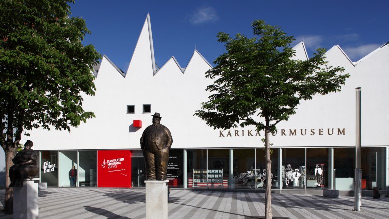 Außenansicht des Karikaturmuseums Krems mit Statuen und Bäumen.