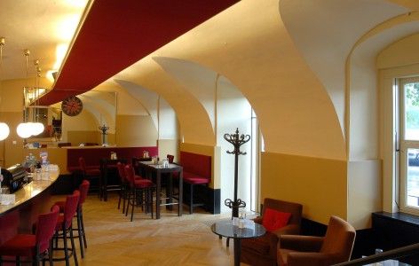Innenansicht eines stilvollen Cafés mit roten Stühlen und gewölbten Decken.