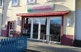 Außenansicht des Mezcal Restaurants mit roten Markisen und Sitzgelegenheiten.