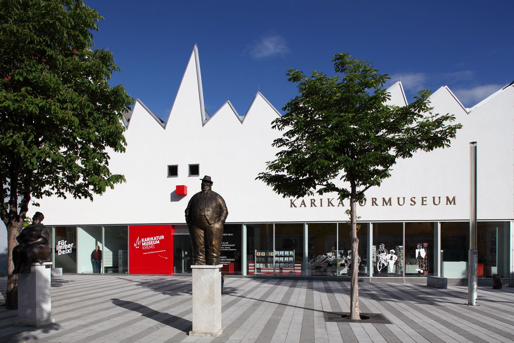 Außenansicht des Karikaturmuseums Krems mit Statuen und Bäumen.