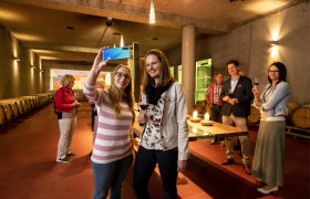 People take a selfie in a wine cellar with barrique barrels.