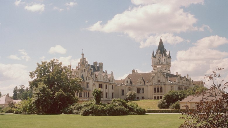 Grafenegg Castle with extensive lawn and trees in the foreground.