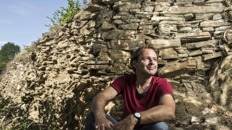 Mann in rotem T-Shirt sitzt vor einer Felswand.