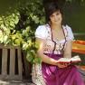 Woman in traditional dress reading a book on a wooden bench under a tree.