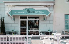 Außenansicht eines Cafés mit Terrasse und Sitzgelegenheiten.