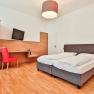 Hotel room with double bed, red chair, desk and TV.