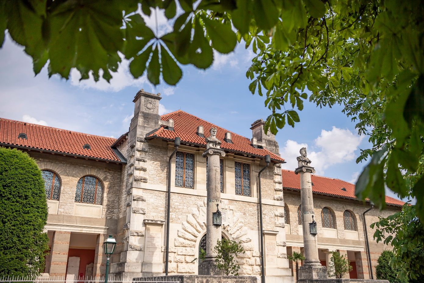Außenansicht des Museums Carnuntinum in Bad Deutsch-Altenburg mit Säulen und rotem Ziegeldach, umgeben von grünen Bäumen.