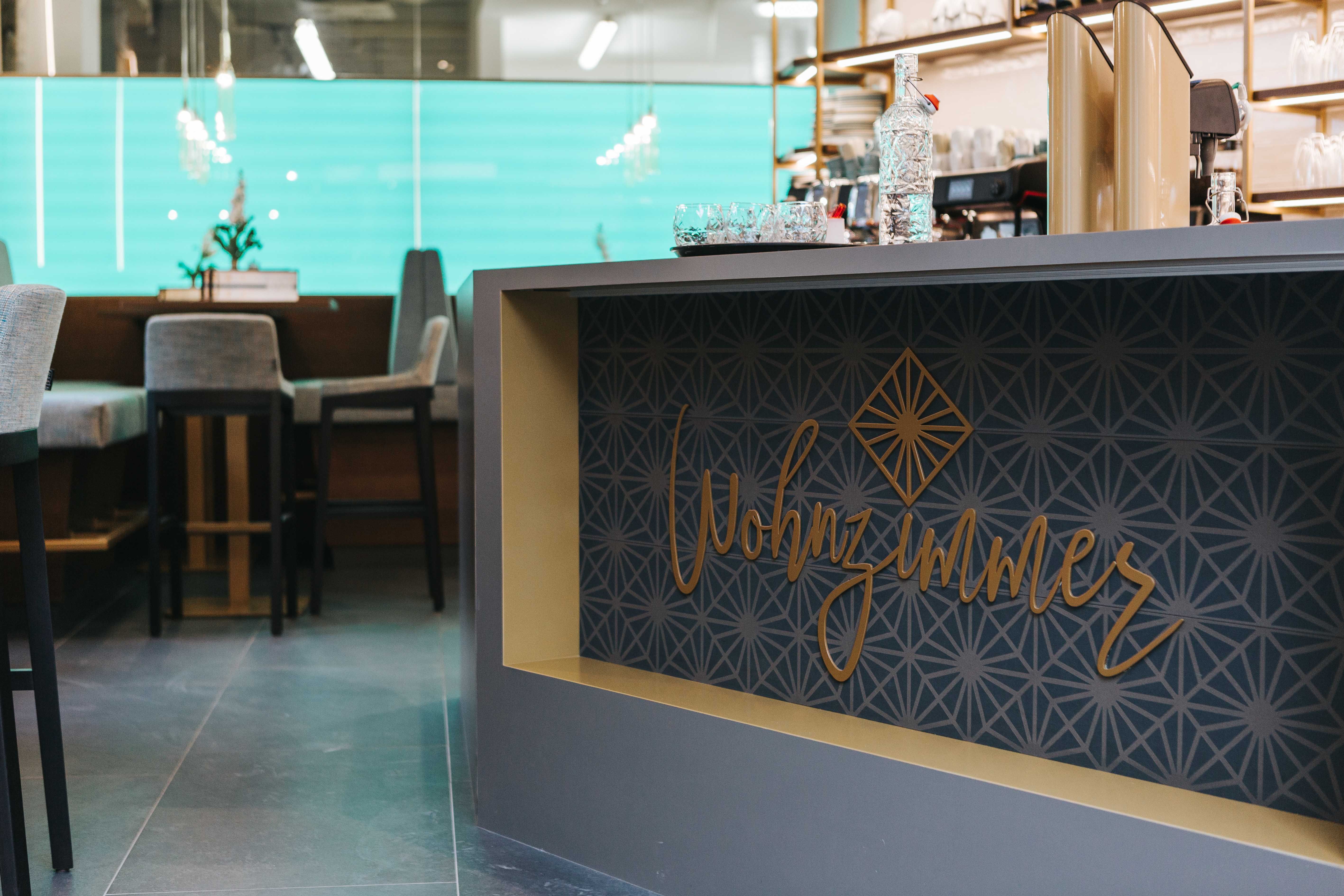 Innenansicht eines Cafés mit dem Schriftzug 'Wohnzimmer' auf einer Theke.