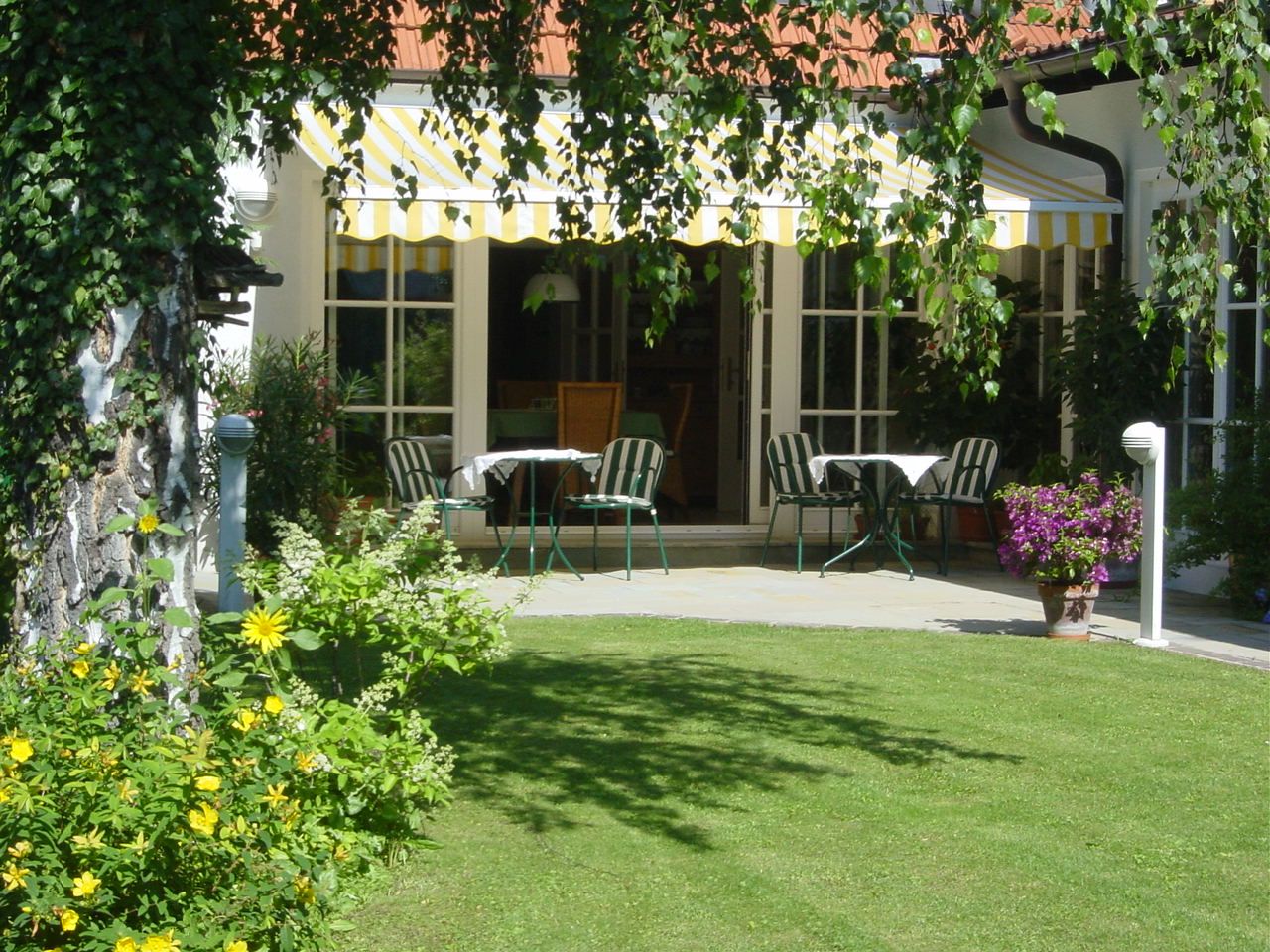 Terrasse mit Gartenmöbeln und Markise, umgeben von Blumen und Rasen.