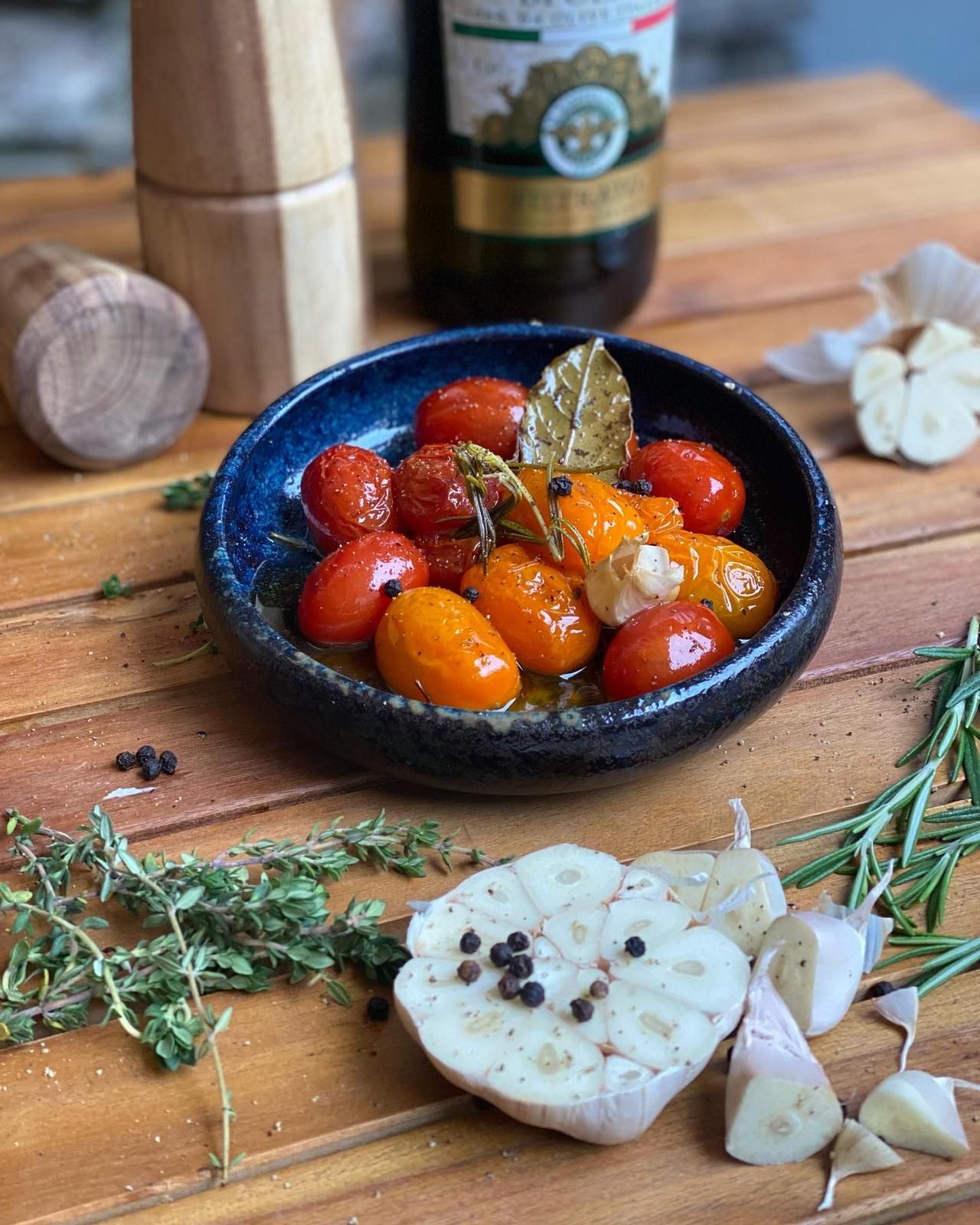 Eine Schale mit confierten Tomaten, Knoblauch und Kräutern auf einem Holztisch.