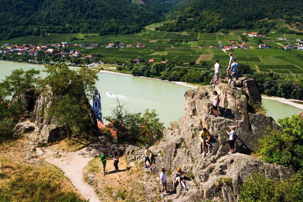 Menschen klettern auf Felsen mit Blick auf die Donau und Weinberge in Dürnstein.