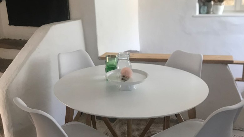 Modern seating area with round table and four white chairs in a bright room.