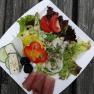 A plate of lettuce, tomatoes, peppers, onions, ham and cheese on a wooden table.